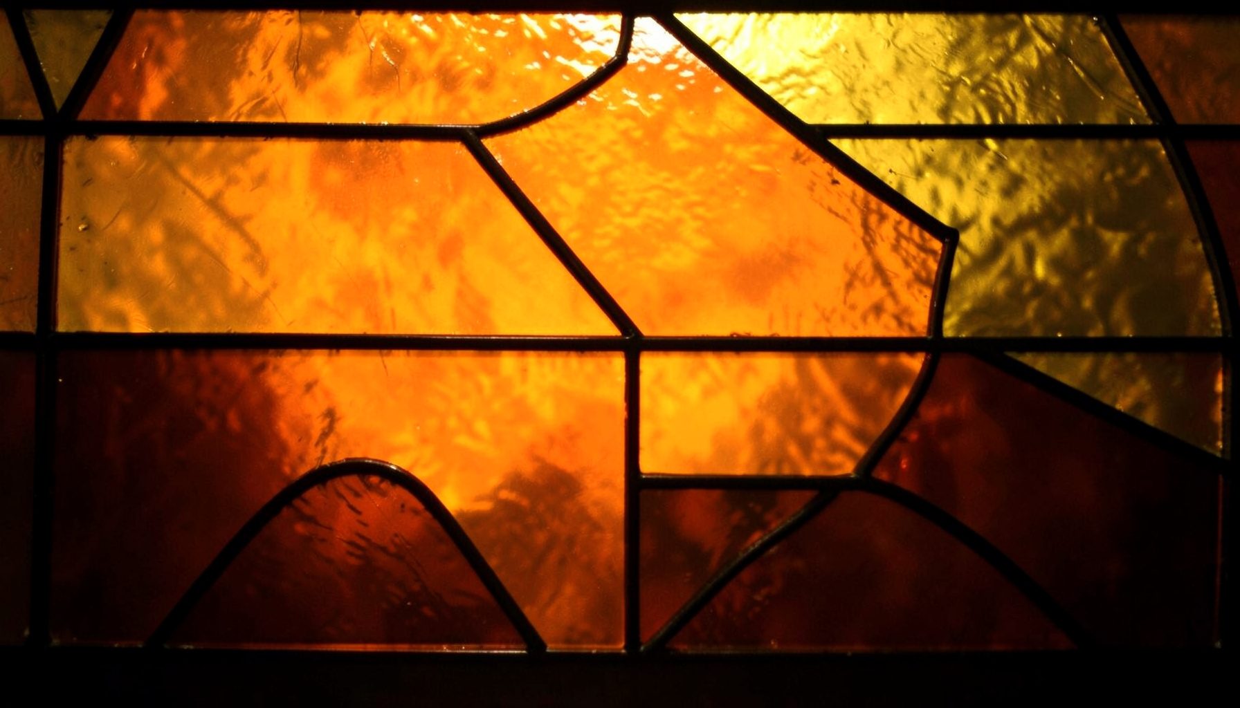A stained-glass composition with bold leaded segments in warm amber, gold, and deep brown tones, radiating a calm and grounded atmosphere